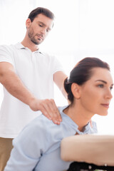Obraz na płótnie Canvas Focused masseur doing shoulders massage of positive female client on blurred foreground