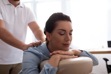 Obraz premium Massage therapist massaging back of positive female client with closed eyes on blurred background