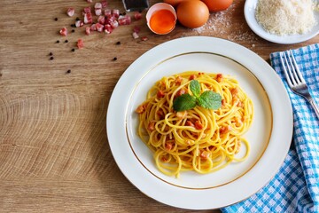 Italian traditional dish "Spaghetti alla Carbonara", spaghetti with yolks,grated parmesan cheeses,smoked bacon and peppers on plate with wooden table background.Easy and tasty food with copy space