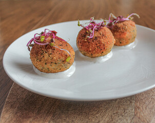 Fancy croquettes over goat cheese sauce. plated on white plate over wooden table. 