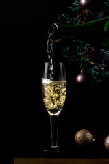 Sparkling wine poured into the champagne glass out of the bottle against the black background. Celebrating Christmas and New Year 
