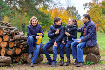family relaxing outdoor in autumn city park, happy people together, parents and children, they drink tea and eat sandwiches, talking and smiling, beautiful nature