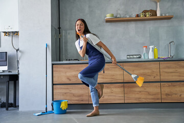 Happy worker. Full length shot of cheerful young woman, cleaning lady pretending to sing a song,...