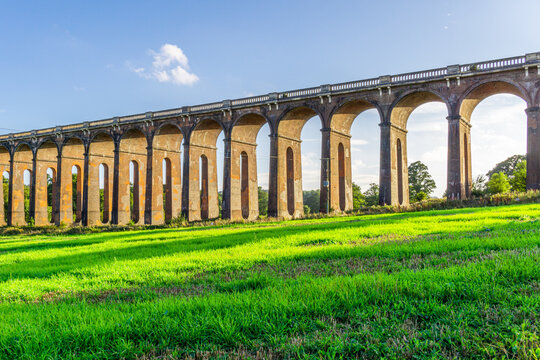 A view of the Ouse Valley Viaduct (Balcombe Viaduct) in the summer with bright sun shining through the arches onto the grass