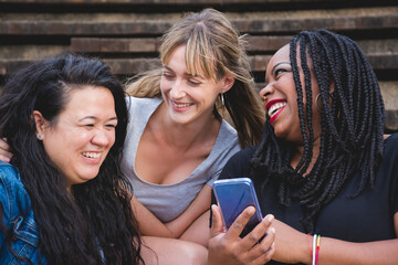 Group of smiling young women of diverse races sharing fun moments using smartphone. Concepts like diversity, friendship, companionship