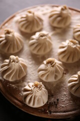 Georgian cuisine. Khinkali. Raw dough with minced meat on a wooden board with flour on a black table. Pepper, cooking process. Background image, copy space