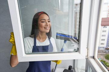 Fast and efficient. Attractive young woman smiling while cleaning the window using squeegee