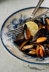 Mussels, clams, seafood in a vintage plate with lemon on a gray concrete background. Top view, copy space