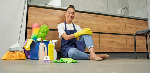 All surfaces clean. Beautiful young woman smiling at camera while resting after cleaning floor with detergents
