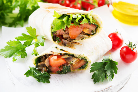 Mexican vegetable burrito wrap tomatoes, lettuce and mushrooms on white background, vegetarian food