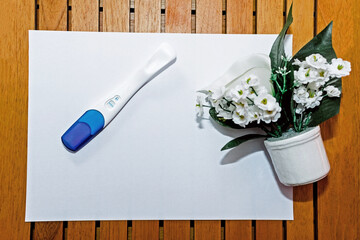 Positive pregnancy test next to some flowers and on top of a white and brown background. Pregnancy test. Pregnancy concept.