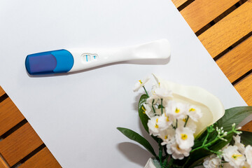 Positive pregnancy test next to some flowers and on top of a white and brown background. Pregnancy test. Pregnancy concept.