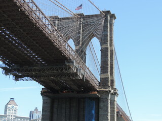 Fototapeta premium El Brooklin Bridge con la Bandera de USA en la torre, que se une con Manhattan (Ney York) visto desde el Crucero de paseo en un dia despejado, 11-05-2014