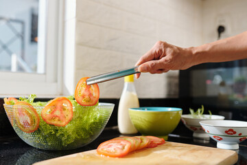 Close-up image of woman putting tomato slices in bowl of dinner salad