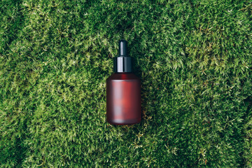 Red matt glass cosmetic bottle on green background, natural moss, grass. Skin care, organic body...