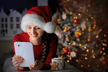 Young girl in a vivid red sweater and Santa hat smiling communicates on the phone with friends before Christmas.