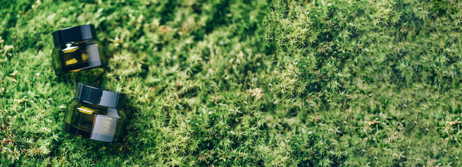 Green glass bottle containers for skincare products on grass, moss background. Skin care, organic cosmetics, body treatment, spa concept. Vegan eco friendly cosmetology product. Biophilia design