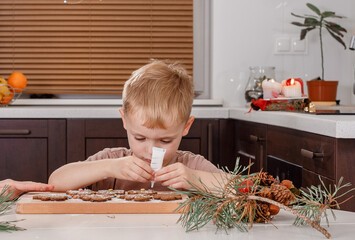 Cute toddler boy decorates Christmas cookies with colorful icing. Seasonal. Boy decorate Christmas cookies for the holiday on wooden table.