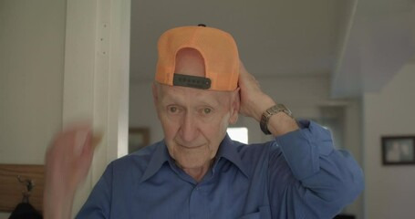 Elderly man puts on backwards hat, close up