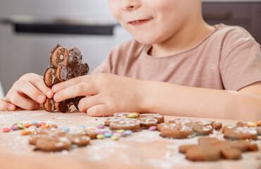 Boy holding a tray full of homemade gingerbread cookies. Kids bake Christmas cookies. Horizontal view of naughty little caucasian kid eating a bite of a chocolate ginger Christmas cookie.