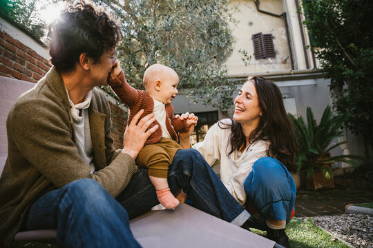 Young happy family having fun together in garden at home at lockdown - Mother and father playing with little baby son in a winter day at sun