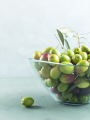 Freshly picked raw green olives in glass bowl on textured background.
