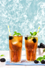 The glass of iced tea with blackberry on wooden table. Cuba Libre or long island cocktail, cold drink or lemonade with lemon and basil. Green turquoise on background