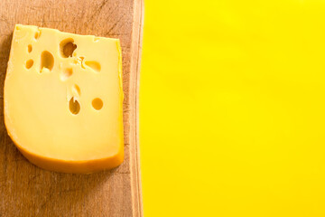 Maasdam cheese on yellow background. Cheese on wooden board. Cheese with copy space.