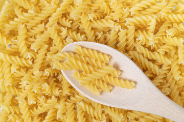 Raw or dry fusilli type of pasta with wooden spoon.