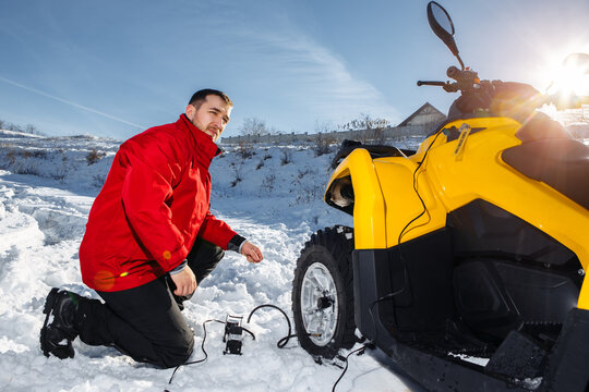 Photo of young man checking air pressure in wheels on the ATV 4wd quad bike stand in heavy snow.