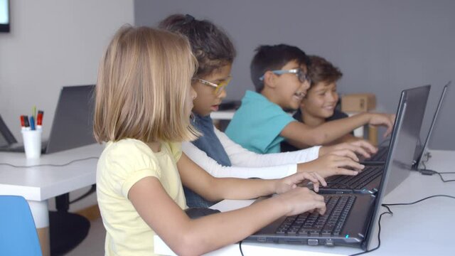 School pupils working on task together, using laptops, typing on keyboard, laughing during computer science class. Side view. Digital education and teamwork concept