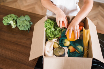 Home food delivery. Various vegetables, fruits and other products in a box that a young girl is...