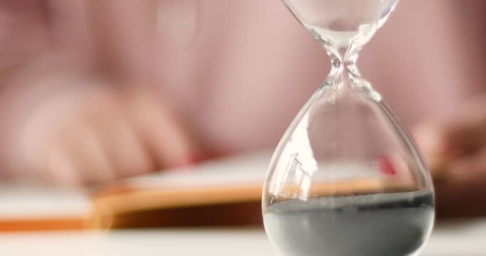 Student girl reads a book, remote study. Sand running through the hourglass.
