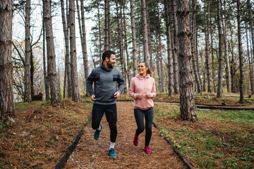 Full length of sporty couple in shape running trough woods at autumn and looking at each other.