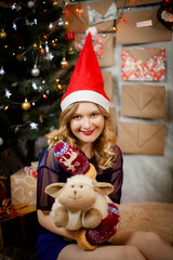 happy smiling girl in red christmas hat and mittens with gifts and toy near decorated christmas tree