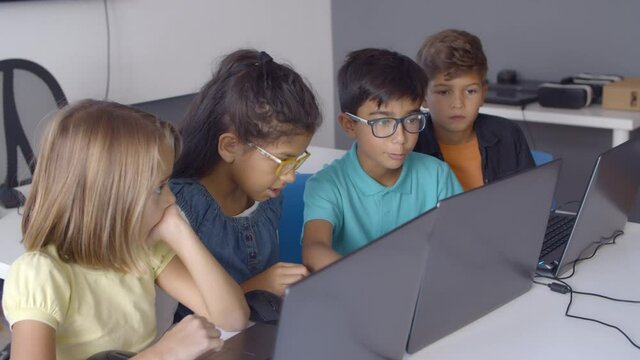 Team of pupils working on task together, sitting at desk and using laptops during computer science class. Side view. Digital education and teamwork concept