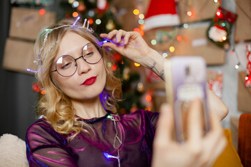funny young Christmas girl taking selfie photo with mobile phone near Christmas tree