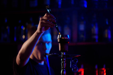 Man smoking traditional hookah pipe and exhaling smoke in hookah cafe.