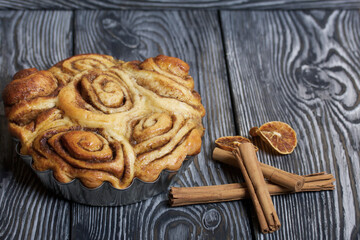 Baked cinnabons in shape. Stand on black composite boards. Nearby are cinnamon sticks. Close-up shot.