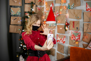 Portrait of a beautiful girl in medical mask, standing in front of decorated christmas tree at home