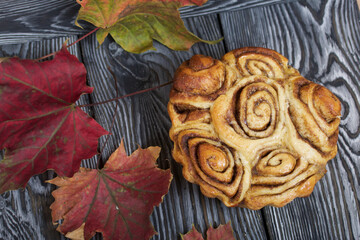 Baked cinnabons in shape. Stand on black composite boards. Nearby are autumn maple leaves.