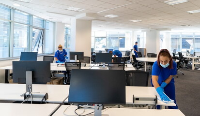 Professional cleaners with the masks on their faces clean and disinfect an empty office space