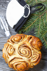 Baked cinnabons in shape. Stand on black pine planks. Nearby are spruce branches, medical masks and an antiseptic.