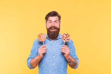 Happy bearded man hold tasty rainbow swirl candy pops great for birthday party and candy buffet yellow background, celebration