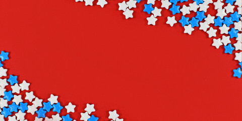 Banner with white and blue star shaped sugar sprinkles on bright red background with blank copy space in middle