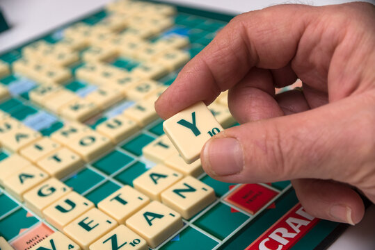 Mulhouse - France - 16 November 2020 - Closeup of hand of woman playing with plastic letter Y to forming a word on Scrabble board game