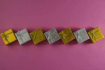 gift boxes of golden and silver color lie on a pink background.
