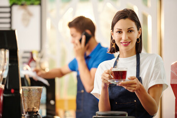 Portrait of pretty smiling female barista holding cup of delicious fresh coffee