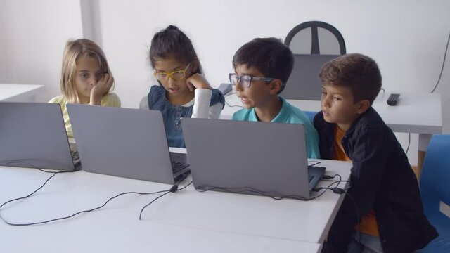 Group of classmates doing task together, sitting at desk and using laptops during computer science class. Front view. Digital education and teamwork concept
