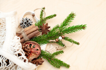 Fototapeta na wymiar Spruce branch in an ecological string bag made of cotton and Christmas decorations on a wooden background. Assortment of cozy hygge Xmas. DIY, zero waste, eco friendly. Flat lay, top view.